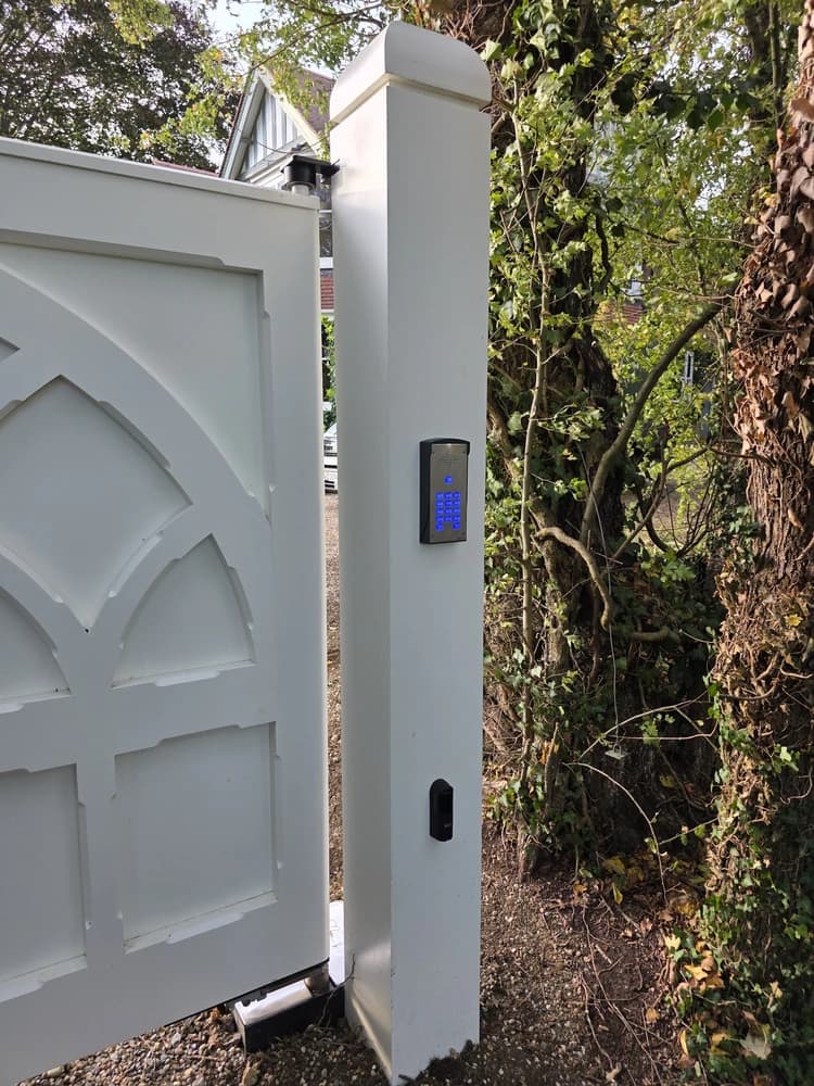 Keypad and intercom mounted beside a white gothic-arch gate